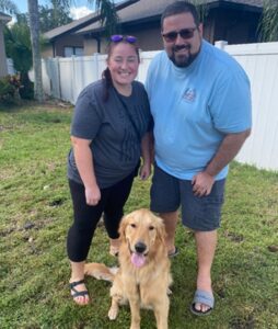 A couple stands with their new golden retriever.