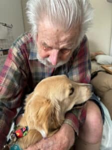 Elderly man gently holding a golden retriever indoors, sharing a tender moment.