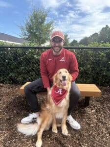 Golden and foster parent sitting with a red bandana around her neck. The bandana is red and has a white "A" in it.