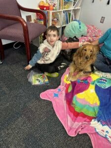 Golden retriever lying on a colorful blanket while a child sitting on the floor pets its head.