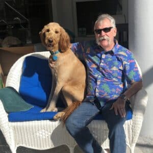 Jerry S. sitting on sofa with Red Sofia, a red goldendoodle.